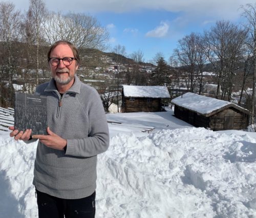 Geir Grøtan viser frem sin bok Namdalsutstillingen, ute på museumsområdet. Snø og skogstuer